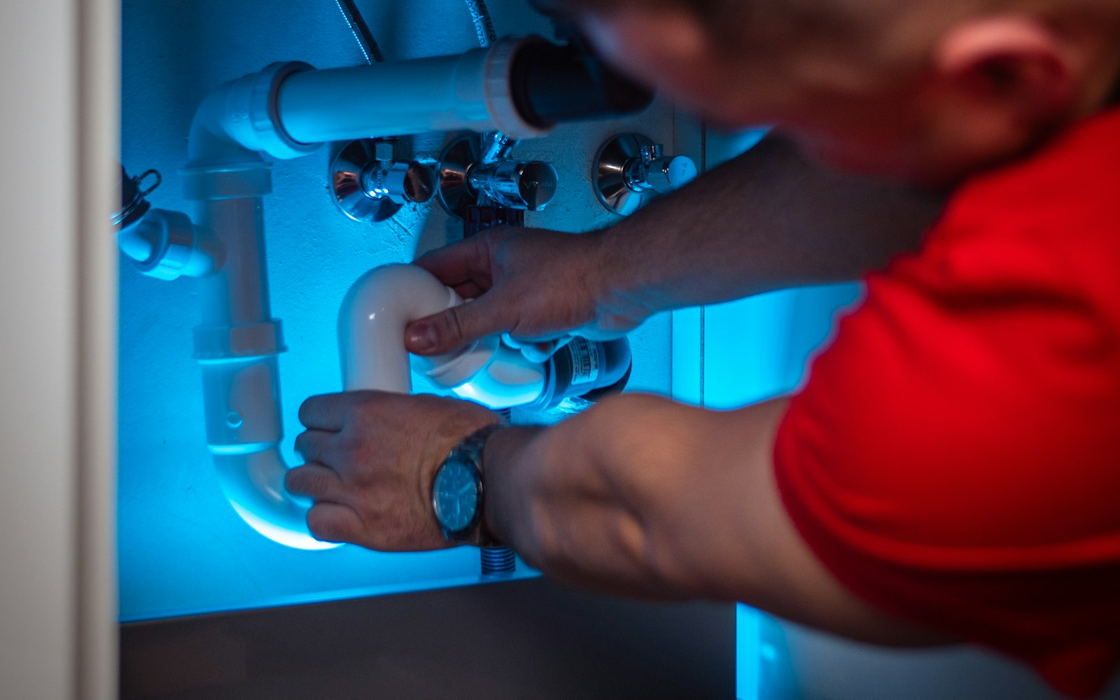 Clogged drain repair: plumber loosening a white PVC P-trap under a sink cabinet